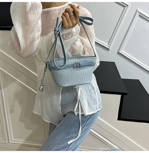 Dettaglio borsa a mano azzurra intrecciata con ciondolo a cuore e tracolla regolabile