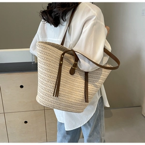 Close-up of beige woven straw tote bag featuring brown leather straps and stylish tassel detail