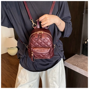 Close-up of a burgundy quilted backpack with gold metal hardware on a model