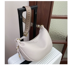 Detail of beige lychee leather crescent bag with a colorful ethnic woven shoulder strap