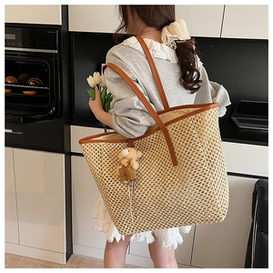 Détail d'un grand sac cabas en paille tressée avec anses en cuir brun et breloque ours