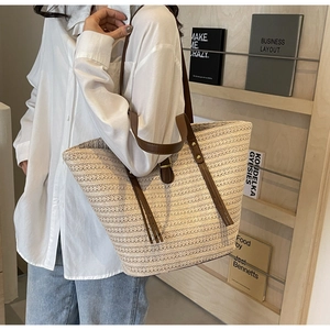 Detail of woven straw tote bag with brown leather straps and decorative tassels