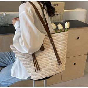 Detail of straw woven tote bag featuring brown leather straps and decorative long tassels