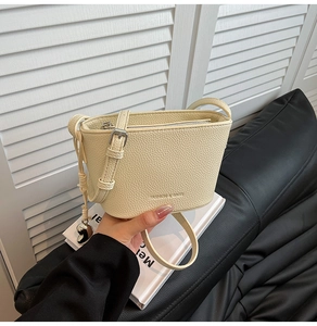Detail der cremeweißen Bucket Bag mit Litschimasertextur, Silberherzanhänger und Metallreißverschluss