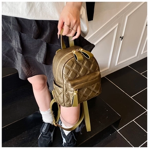 Detail of olive green quilted mini backpack with gold hardware on indoor stairs