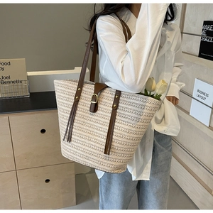 Straw tote bag detail with brown leather straps, gold hardware and fringe accent