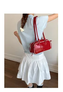 Red leather baguette shoulder bag with white piping and ribbon bows on model