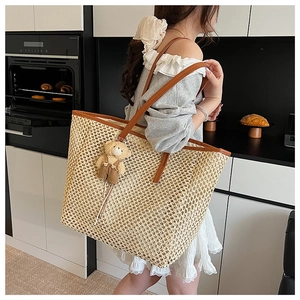 Détail d'un sac cabas en paille évidée avec bandoulière en cuir brun et pendentif ours