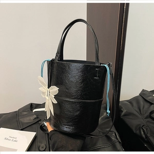 Detail of black glossy bucket bag with crinkled texture and white 3D flower charm