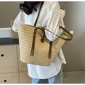 Detail of straw woven tote bag with brown leather straps and metal buckle accents
