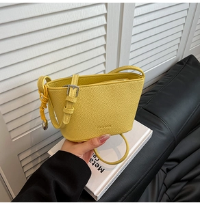Detail der gelben Beuteltasche aus strukturiertem Leder mit FASHION-Prägung und Silberschnalle