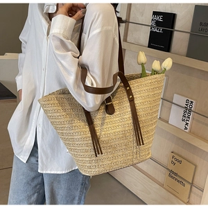 Detail of woven straw tote bag with brown leather strap and decorative side tassels