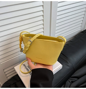 Detail der gelben Leder-Eimertasche mit Lychee-Muster, silbernen Beschlägen und Mode-Logo