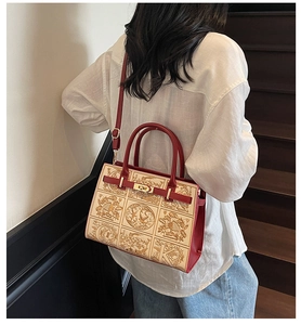 Detailed back view of an embroidered handbag with gold animal patterns and red strap