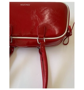 Close-up of shiny red faux leather handbag with white trim and bow tie detail
