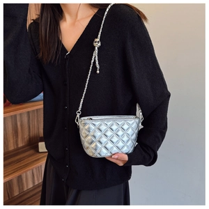 Detail of silver quilted mini bucket bag with metallic chain strap worn by a model