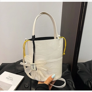 Detail of white bucket bag featuring yellow drawstrings and a white floral charm