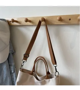 Detail of beige canvas tote with brown straps and adjustable shoulder strap on wall hook