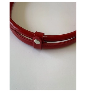 Detail of red glossy leather bag featuring silver metal snap fastener and stitching