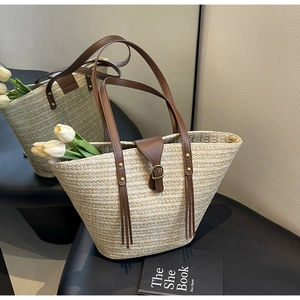 Detail of woven straw tote bag featuring brown leather straps with gold rivets and buckle