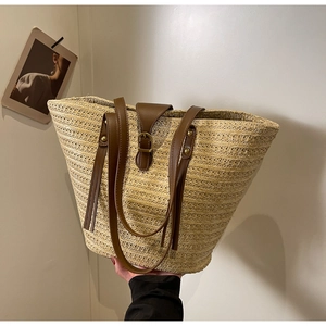 Detailed close-up of straw woven texture with brown leather flap and tassel on tote bag