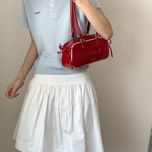 Detail of red patent leather baguette bag featuring white trim and bow accents on strap