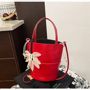 Detail of red bucket bag showing pleated leather texture, flower pendant, and embossed logo