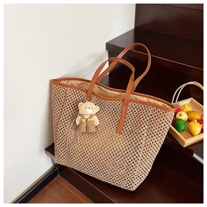 Détail d'un sac cabas en paille tissé à la main avec anses en cuir brun et breloque ours