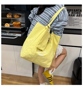 Detail view of the large yellow tote bag with white artistic lettering and long shoulder strap