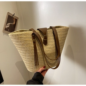 Detail of hand-woven straw tote bag showing brown leather handles and decorative tassels