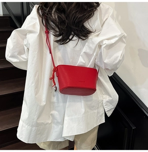 Nahaufnahme einer roten Leder-Eimertasche mit geprägtem Fashion-Schriftzug und Metallanhänger