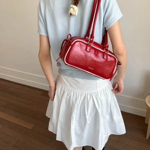 Detail of red faux leather baguette bag with white trim shown on a female model