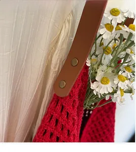 Detail of red hollow knit tote bag showing brown leather strap with bronze rivets
