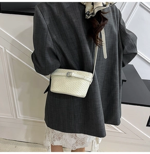 Borsa a tracolla intrecciata color crema indossata da una modella con completo grigio