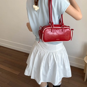 Detail of red faux leather cylinder bag with white piping and side ribbon bows