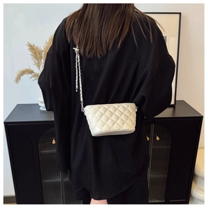 Detail of cream quilted crossbody bag with silver chain strap and diamond stitch texture