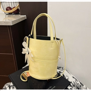 Detail of light yellow bucket bag with floral charm and textured faux leather finish