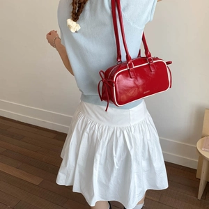 Detail view of red glossy leather shoulder bag with bow drawstring and white trim edges