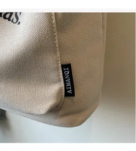 Detailed close-up of cream canvas tote bag with side label and black letter printing