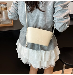 Detail der cremeweißen Beuteltasche mit Litschi-Struktur und feinem Riemen am Outfit