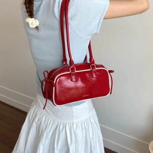 Detail shot of the red faux leather baguette bag showing white piping and bow detail