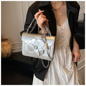 Detail view of silver floral handbag featuring 3D camellia decor and pearl chain strap