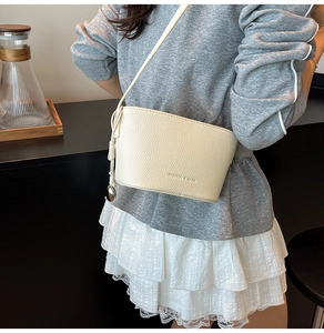 Detail der cremeweißen Eimertasche aus Litchi-Leder mit Metallkugel-Anhänger und Trageriemen