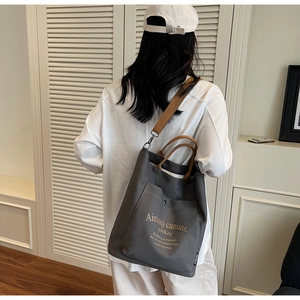 Detail of grey canvas tote bag with brown straps and large front pocket on a model