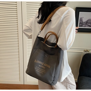 Detailed view of grey canvas tote bag with brown straps and side logo label