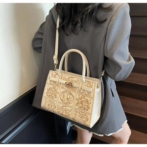 Detailed embroidery and gold clasp on a beige crossbody bag worn by a model on stairs