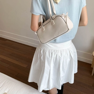 Detail of a creamy white faux leather baguette bag with a side bow and slim straps