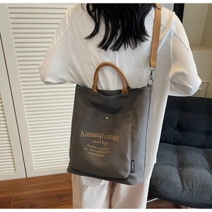 Detail of dark gray canvas tote bag featuring brown handles and retro letter printing