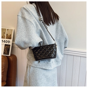 Detail of black quilted chain bag with a metal adjustment ball shown on a shoulder