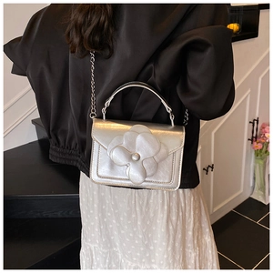 Silver chain bag featuring a large 3D camellia flower seen from the back on a model